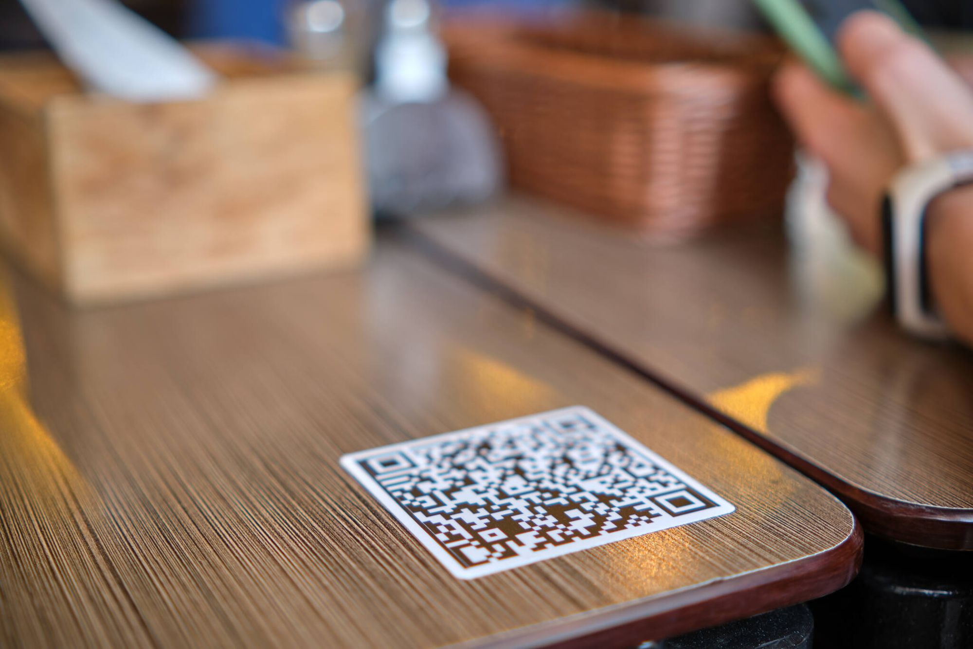 a QR code on a wooden table and a hand next to it