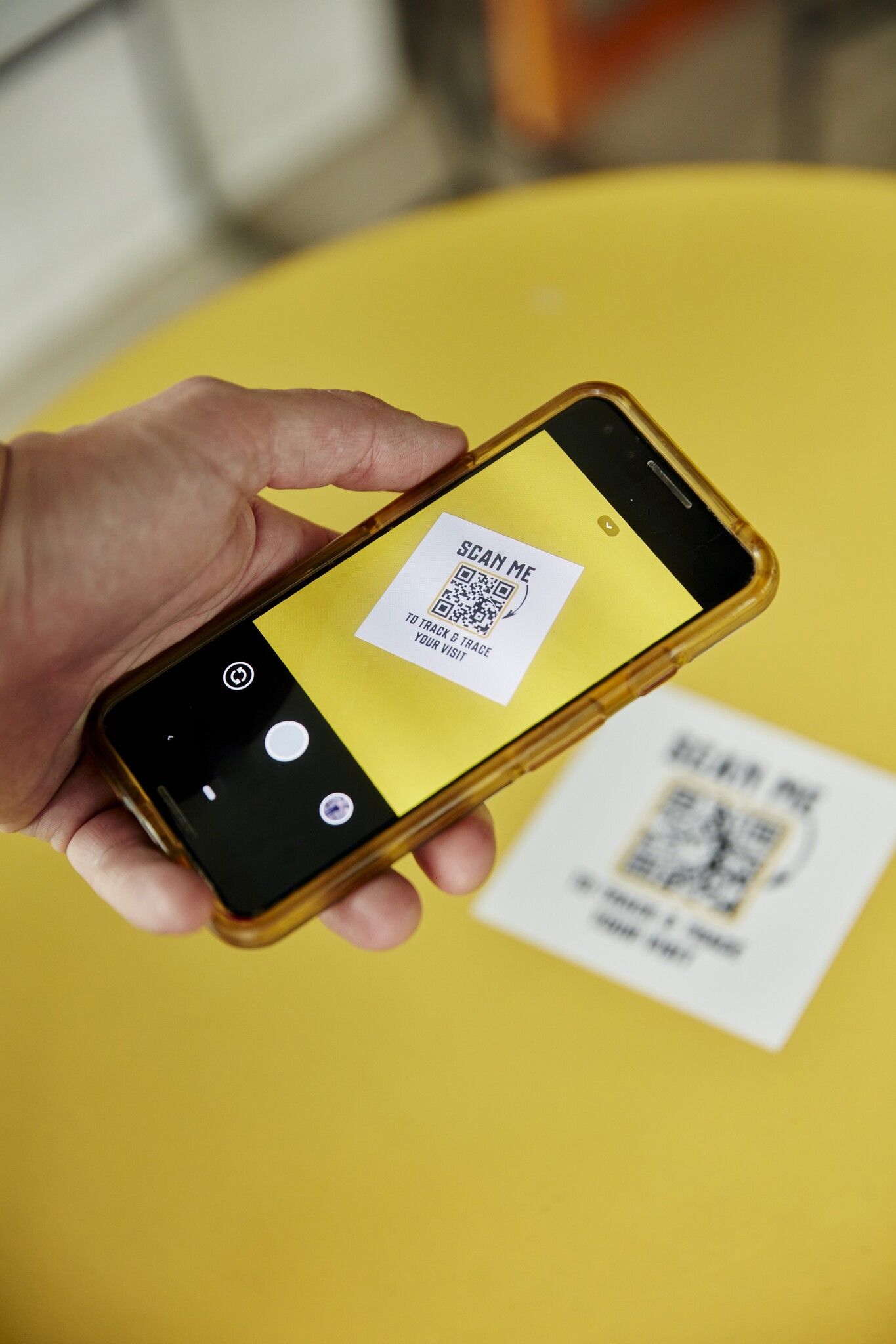 a hand scanning a QR code with a phone that says "to track and trace your visit"