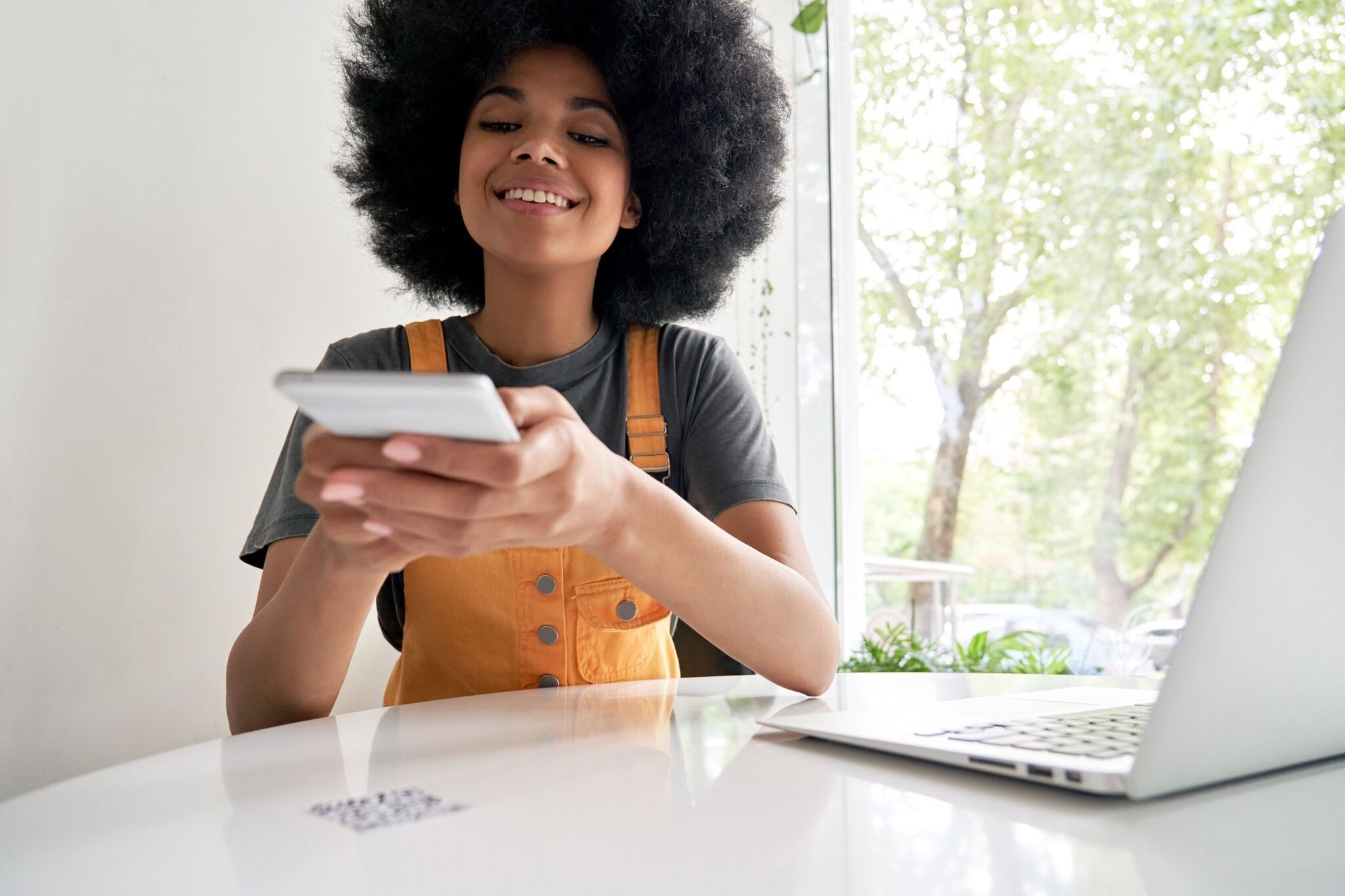 a girl wearing overalls scanning a QR code and smiling