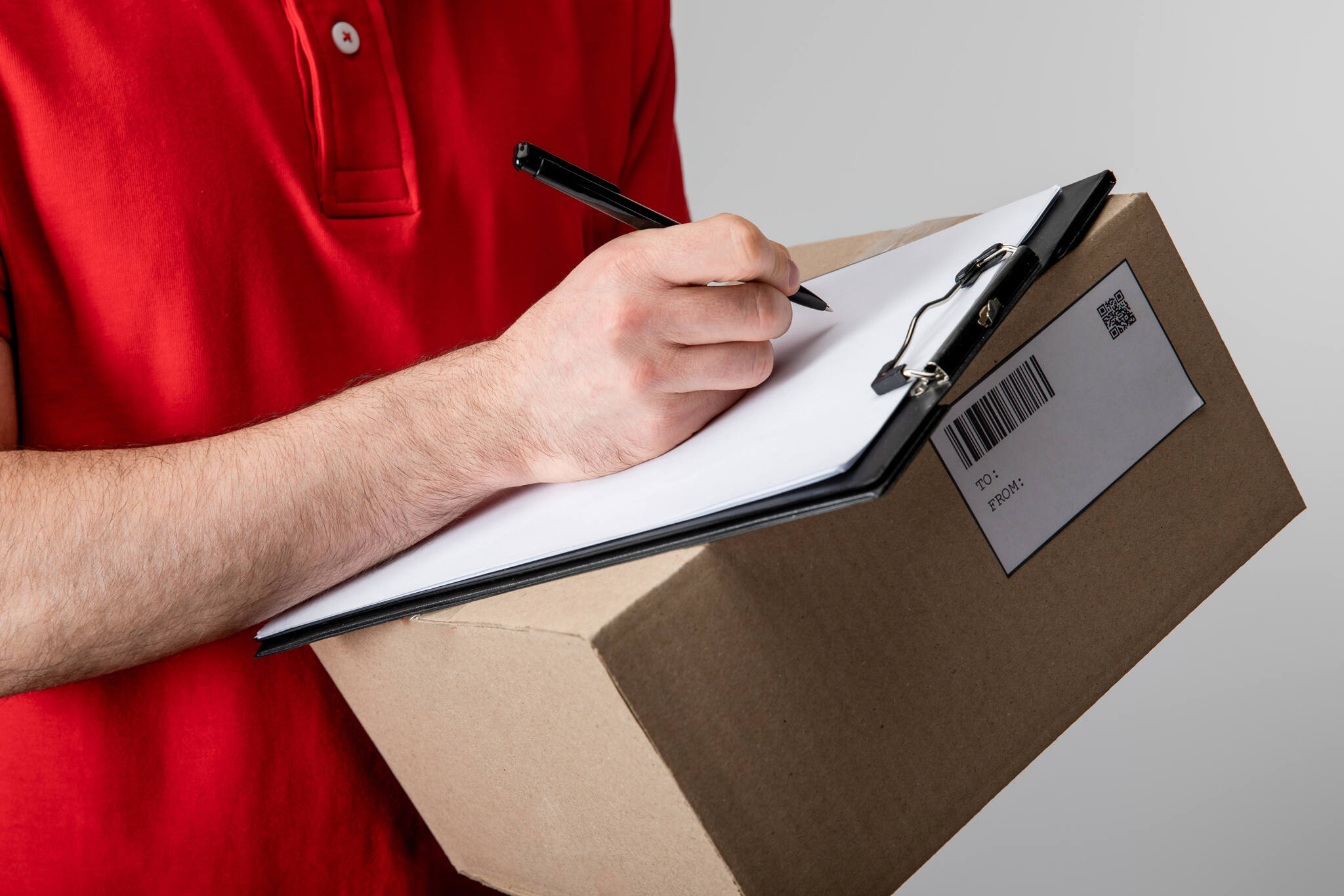 cropped view of courier writing on clipboard and a package with QR code and barcode