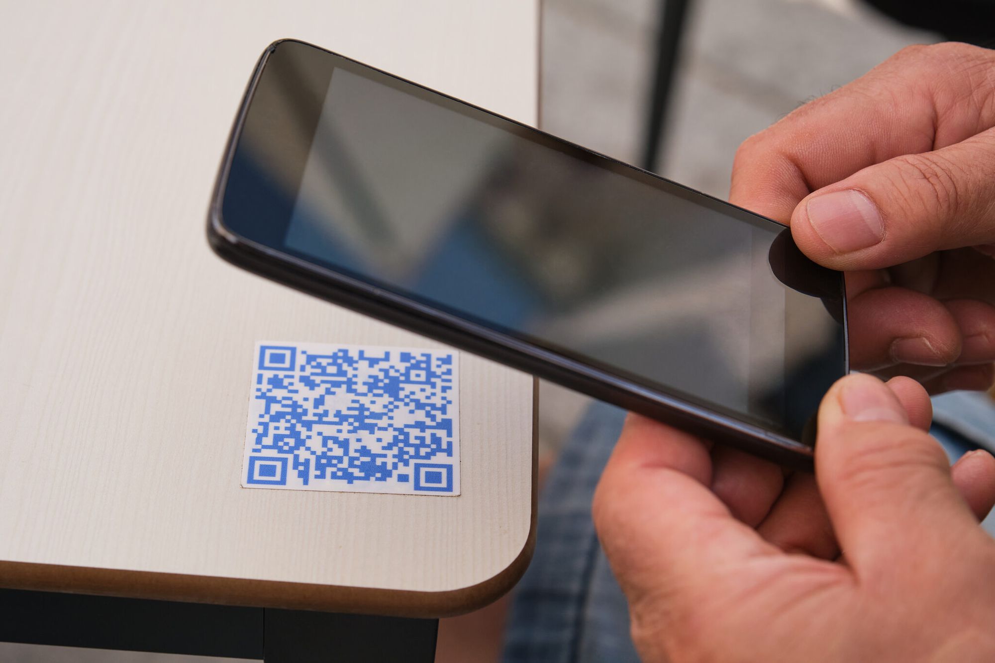 man hand using the smartphone to scan a blue QR code on a table