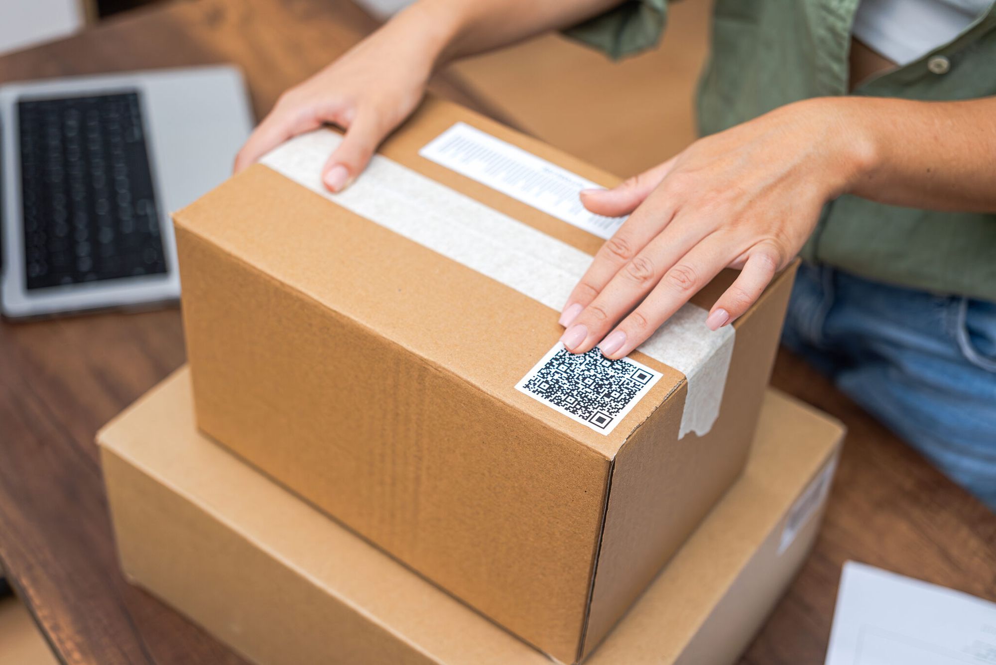 Close-up of woman's hands adding a QR code sticker to a package