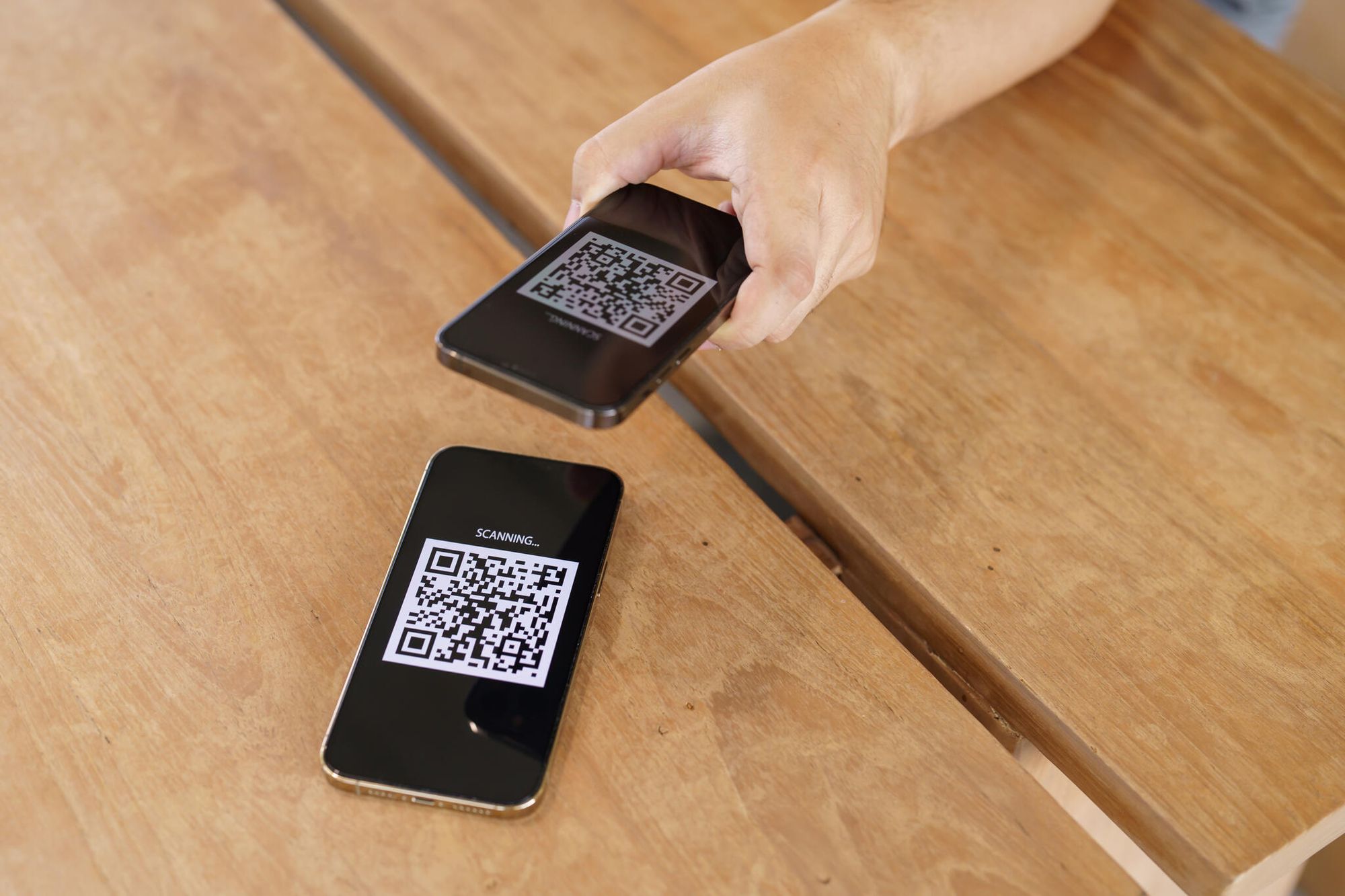 a phone scanning a QR code on another phone on a wooden table